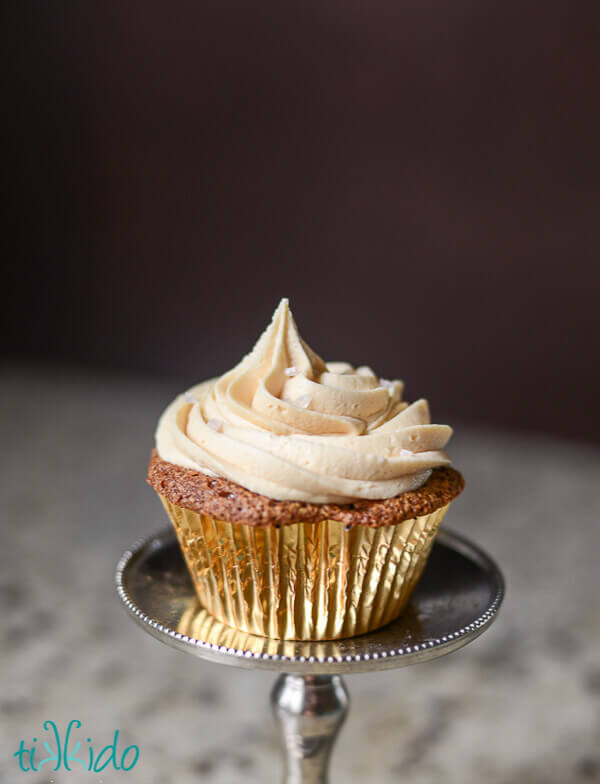 Cupcake in a golden wrapper topped with salted caramel frosting.