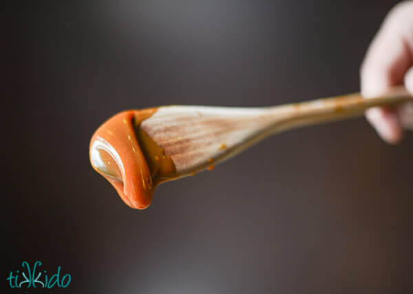 Wooden spoon with salted caramel sauce dripping off the end, ready to be used to make Salted Caramel Frosting.
