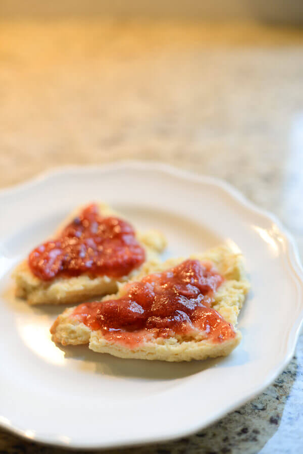 Strawberry freezer jam spread on two halves of a split scone, on a white plate.