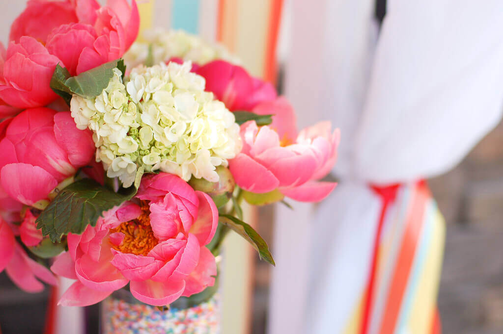 Pink peonies and white hydrangeas in a vase lined with rainbow sprinkles.