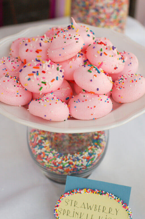 Sprinkles-filled vase holding a plate of pink meringues with rainbow sprinkles.
