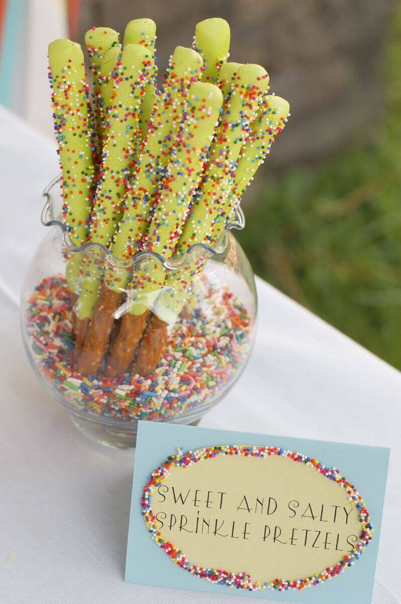 Frosting covered pretzels displayed in a vase full of sprinkles.