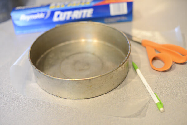 Round cake pan being lined with waxed paper to make a homemade strawberry cake recipe.