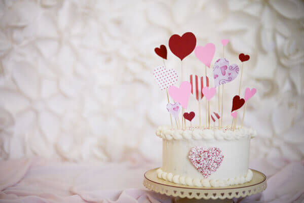 Strawberry cake iced in cream cheese icing and decorated with heart cake toppers for Valentine's Day.