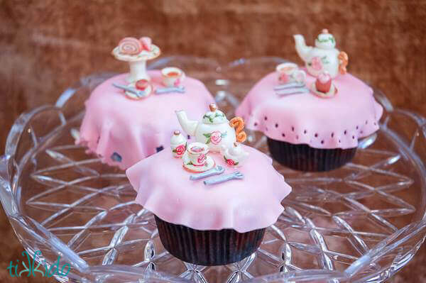 Three tea party cupcakes featuring miniature tea settings made out of gum paste.