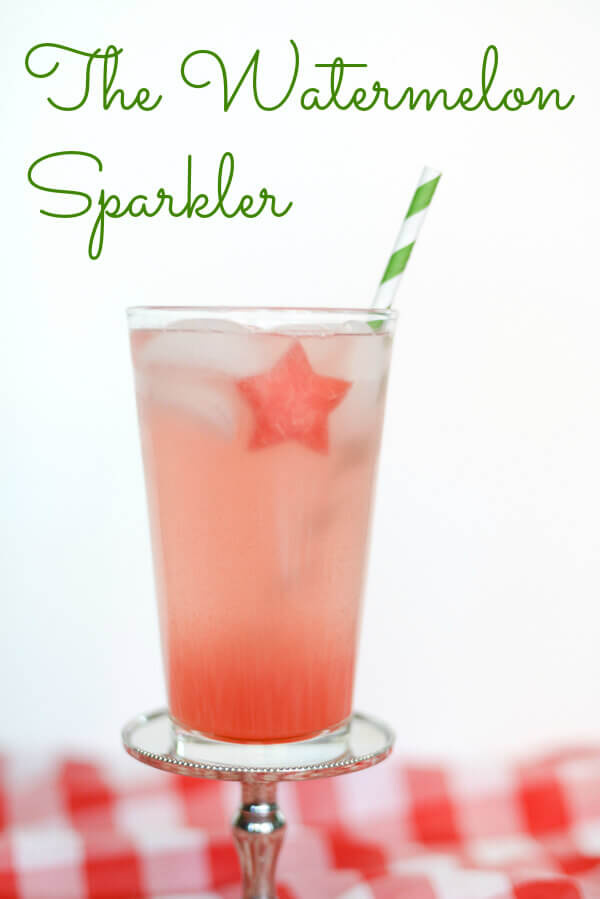 Pink watermelon drink with a star shaped piece of watermelon in a tall glass, with a green striped paper straw, on a white background.