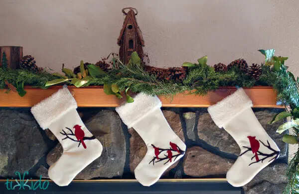Real evergreen garland on a fireplace mantel, with three Christmas stockings hanging from the mantel.