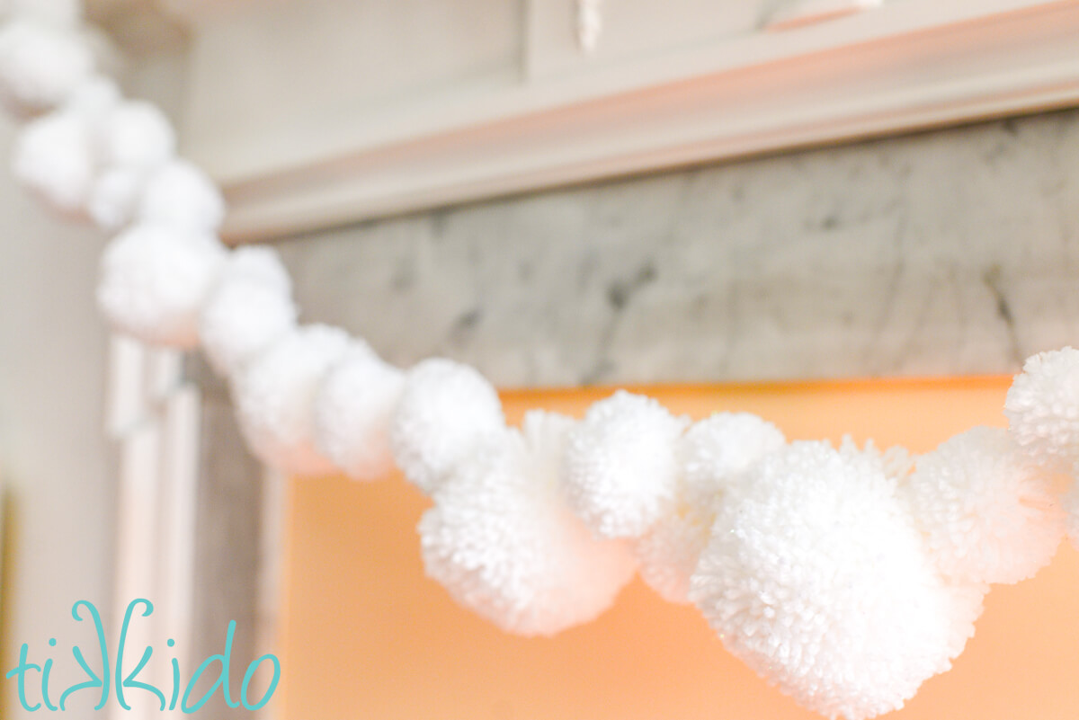 Pom pom garland made from white yarn hanging on a fireplace mantel.