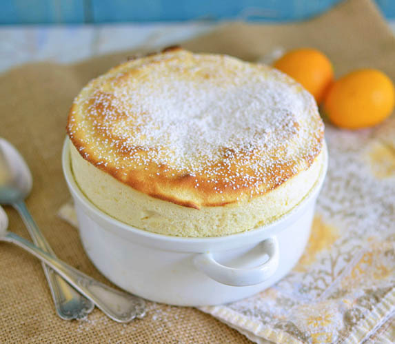 Meyer Lemon souffle in a white baking dish, sprinkled with powdered sugar, next to two lemons and two spoons.