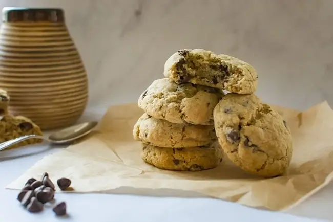 Stack of thick, vegan chocolate chip cookies made with rye flour on tan parchment paper.