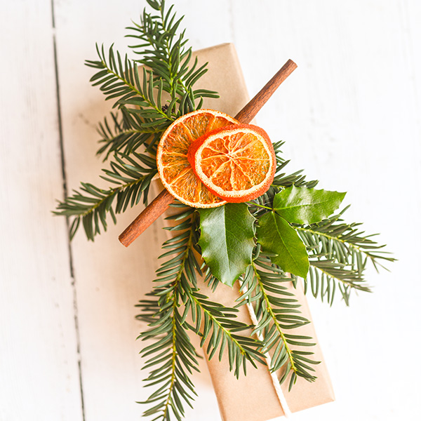 Present wrapped in brown kraft paper, tied with white string, and decorated with a gift topper made from dried orange slices, cinnamon sticks, and fresh greenery.