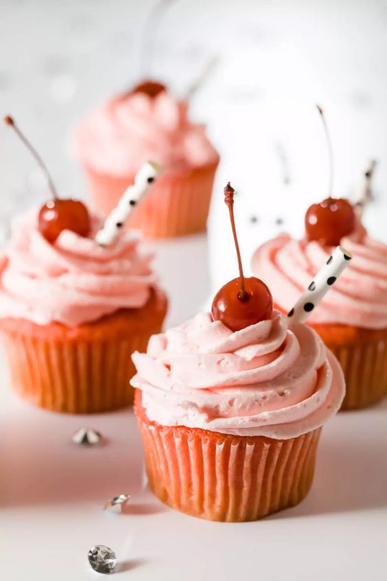 Shirley temple cupcakes topped with a maraschino cherry and paper straw.