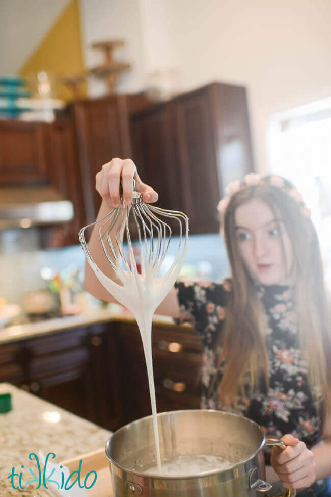 Young girl holding a whisk dripping Homemade Marshmallow fluff into a mixing bowl
