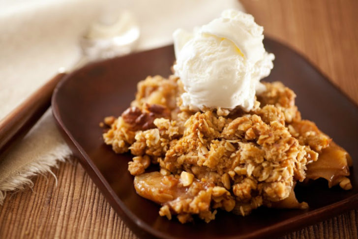 Crockpot apple crisp on a dark square plate, topped with a scoop of vanilla ice cream.