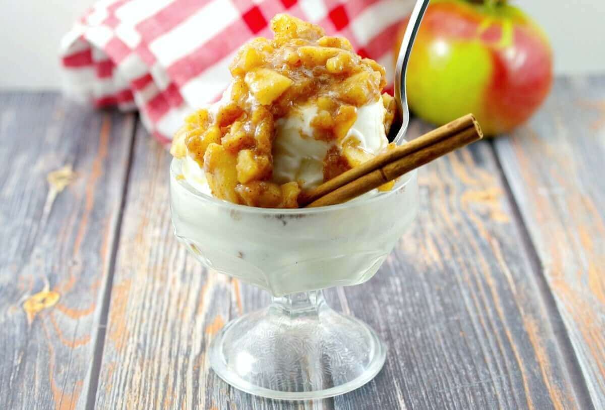 Apple cinnamon ice cream topping on top of vanilla ice cream, in a glass ice cream bowl garnished with a cinnamon stick.