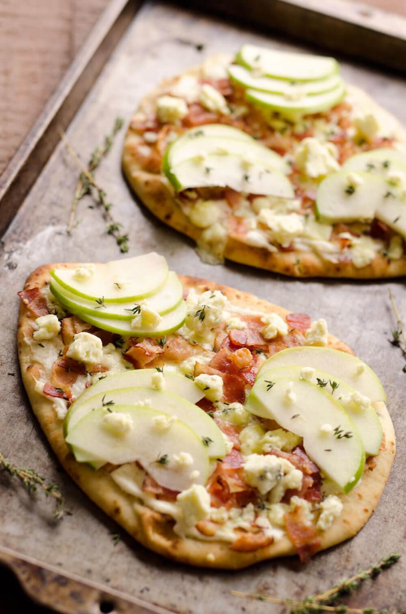 Bacon, bleu cheese, and apple flatbread appetizer on a parchment lined baking sheet.