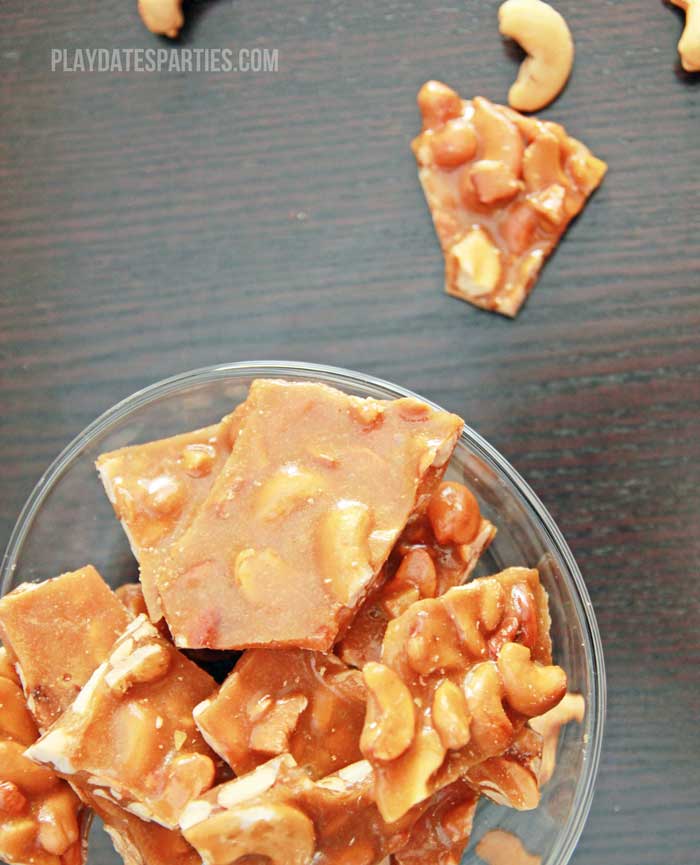 Pieces of brown sugar cashew brittle in a clear bowl on a dark wood table.