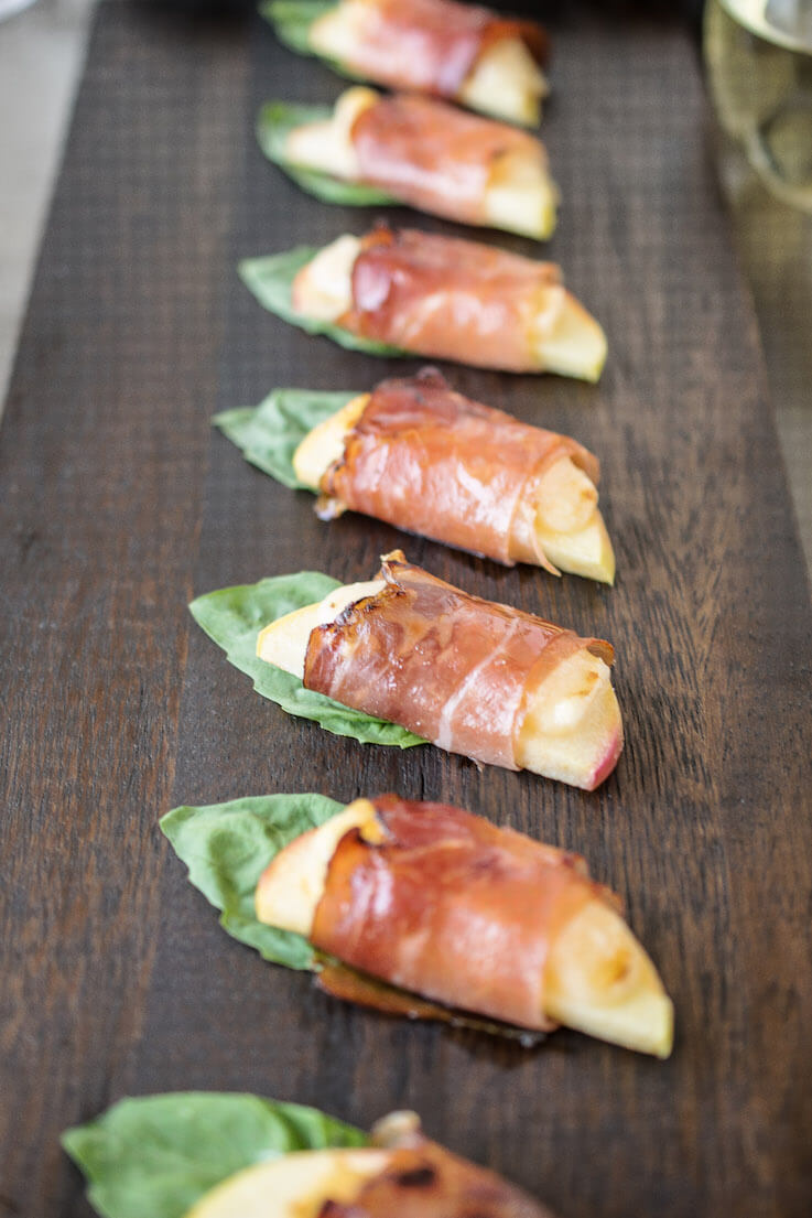 Smoked Prosciutto wrapped apple appetizers with fresh basil on a wooden serving tray.