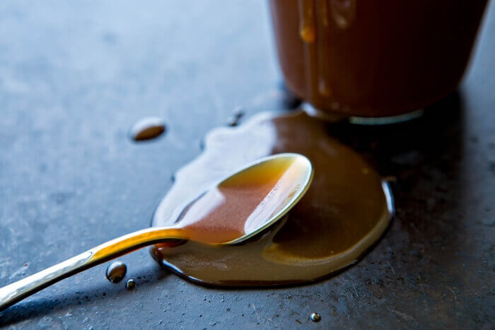 Vanilla bourbon caramel sauce  Ice Cream Topping puddled around a spoon on a dark grey surface.