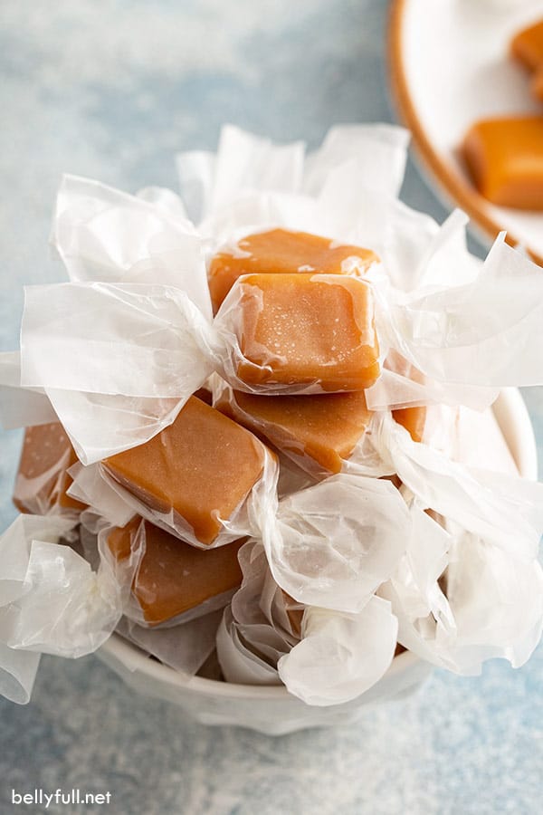 Soft caramels made with evaporated milk, wrapped in waxed paper, in a white bowl.