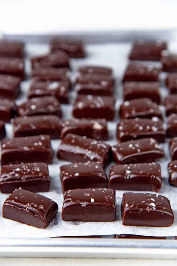 Squares of chocolate caramels sprinkled with sea salt on a parchment lined baking tray.