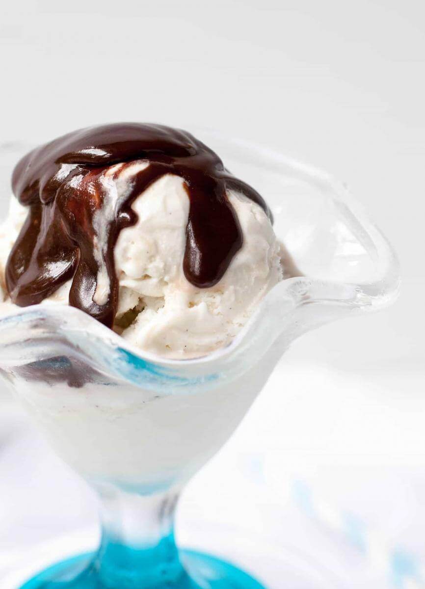 Chewy hot fudge sauce on vanilla ice cream in a glass ice cream dish.