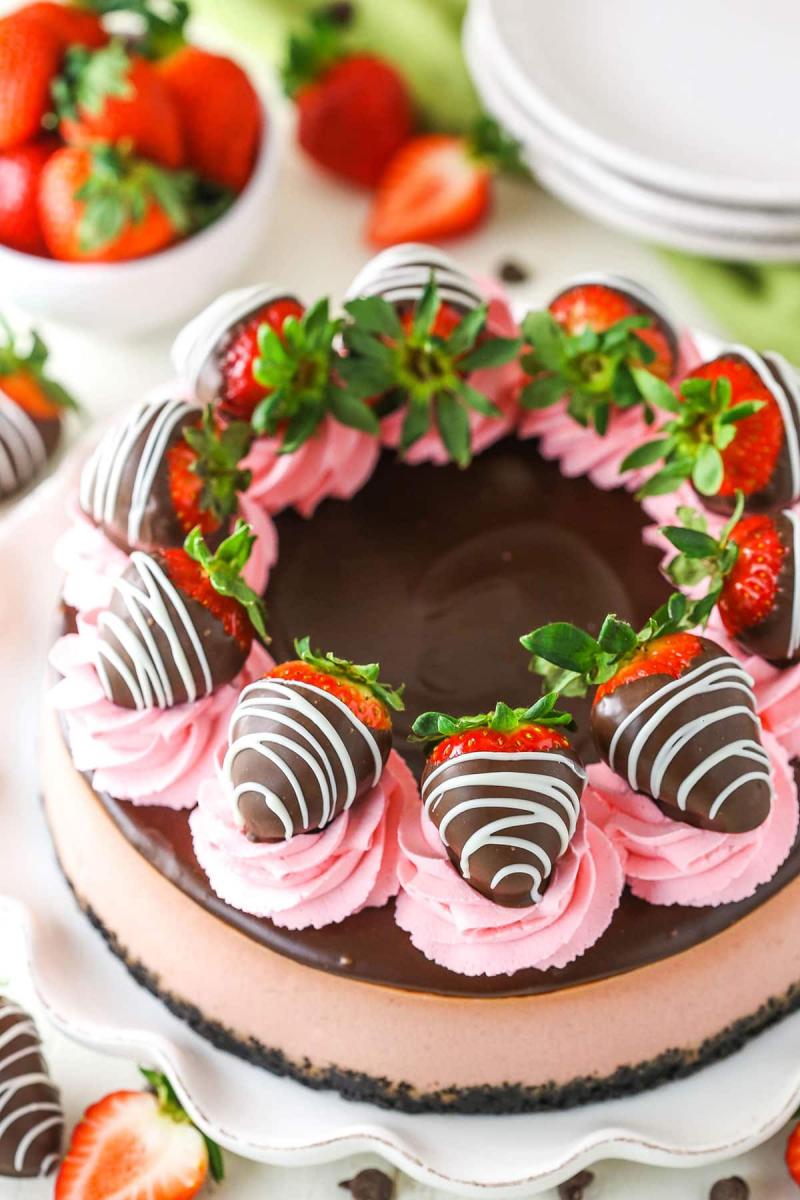 Chocolate covered strawberry cheesecake decorated with swirls of pink strawberry frosting and chocolate covered strawberries.