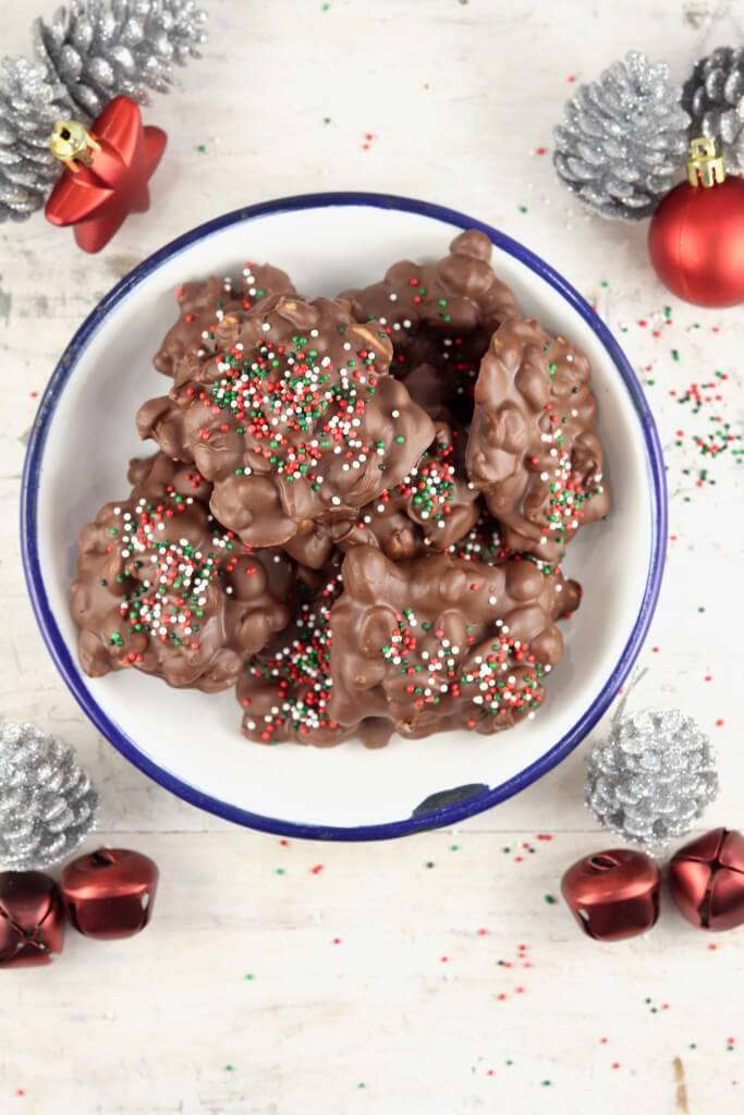 Chocolate peanut butter cluster candies on a white plate surrounded by Christmas decorations.
