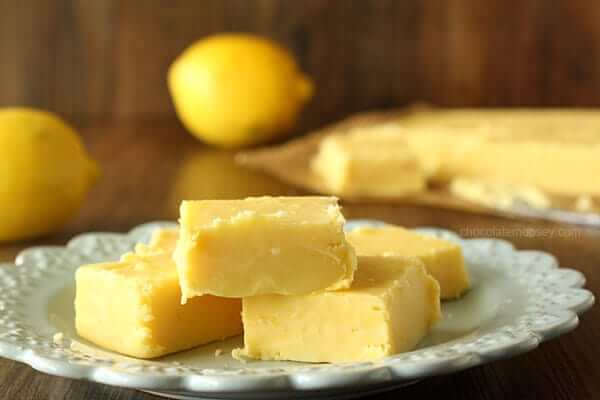 Pieces of lemon fudge on a white plate, with whole lemons in the background.