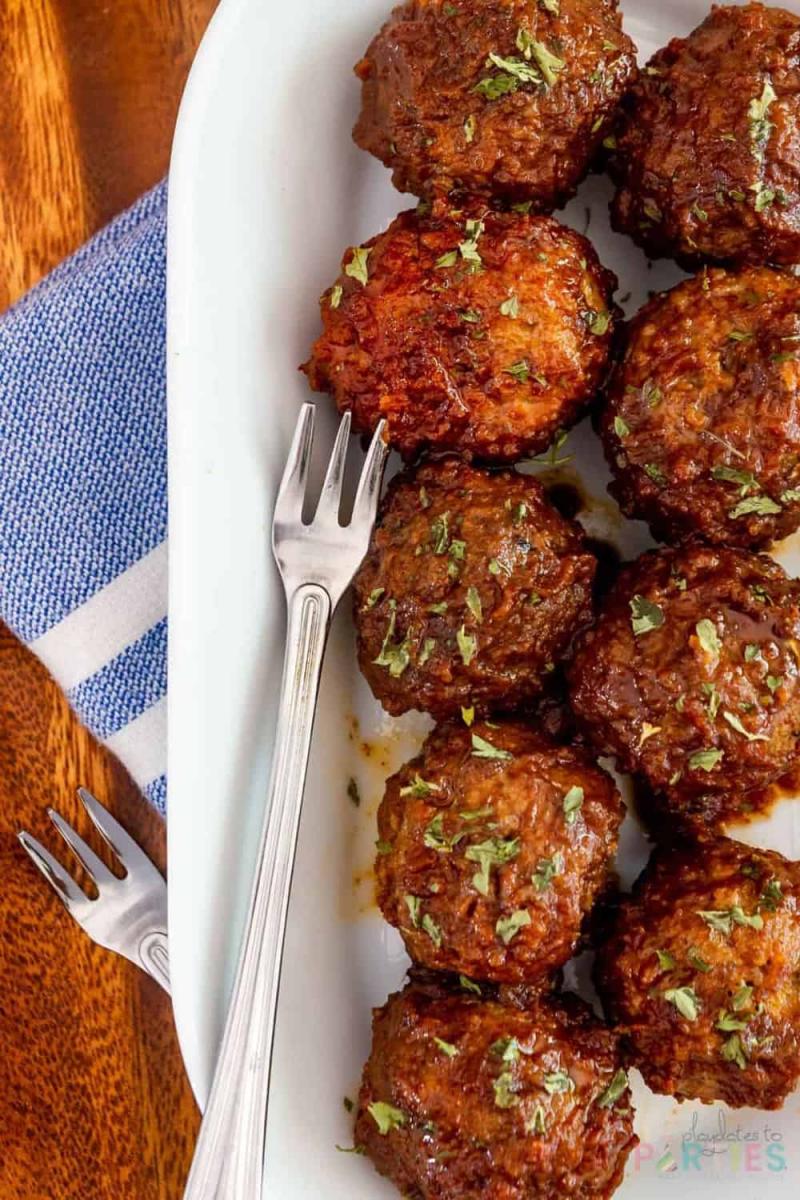 Crockpot apple butter meatballs with bourbon on a white serving tray with a small serving fork.