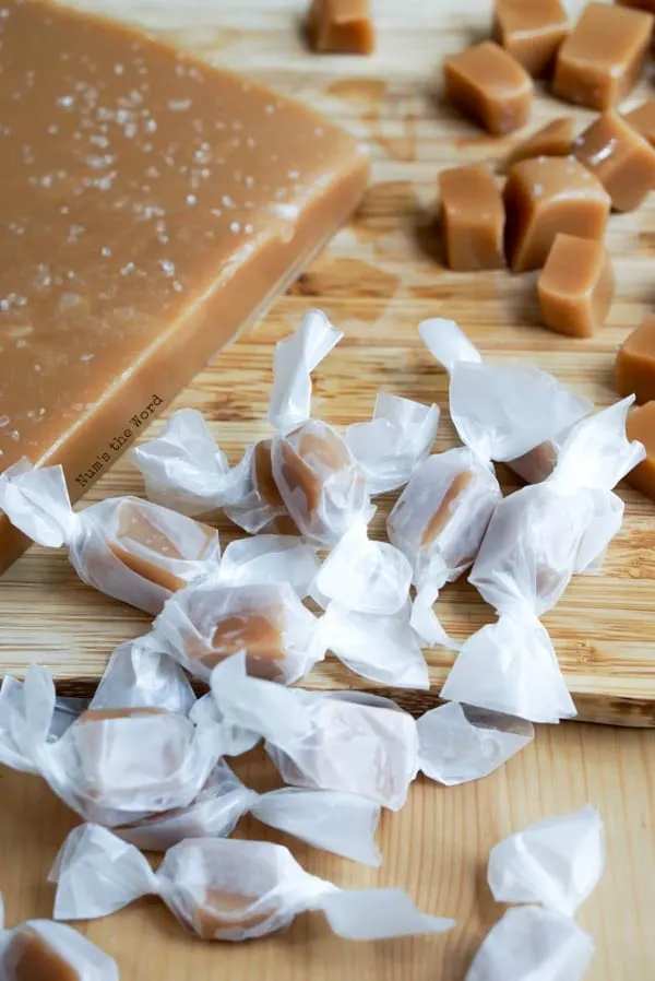 Maple Christmas caramels wrapped in waxed paper on a wooden cutting board.