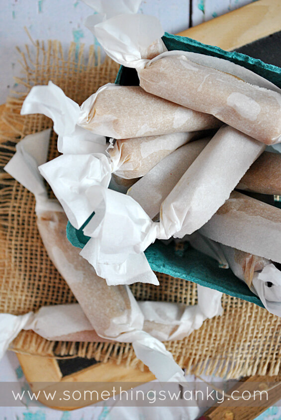 Peanut butter caramels wrapped in parchment paper in a blue container on top of burlap.