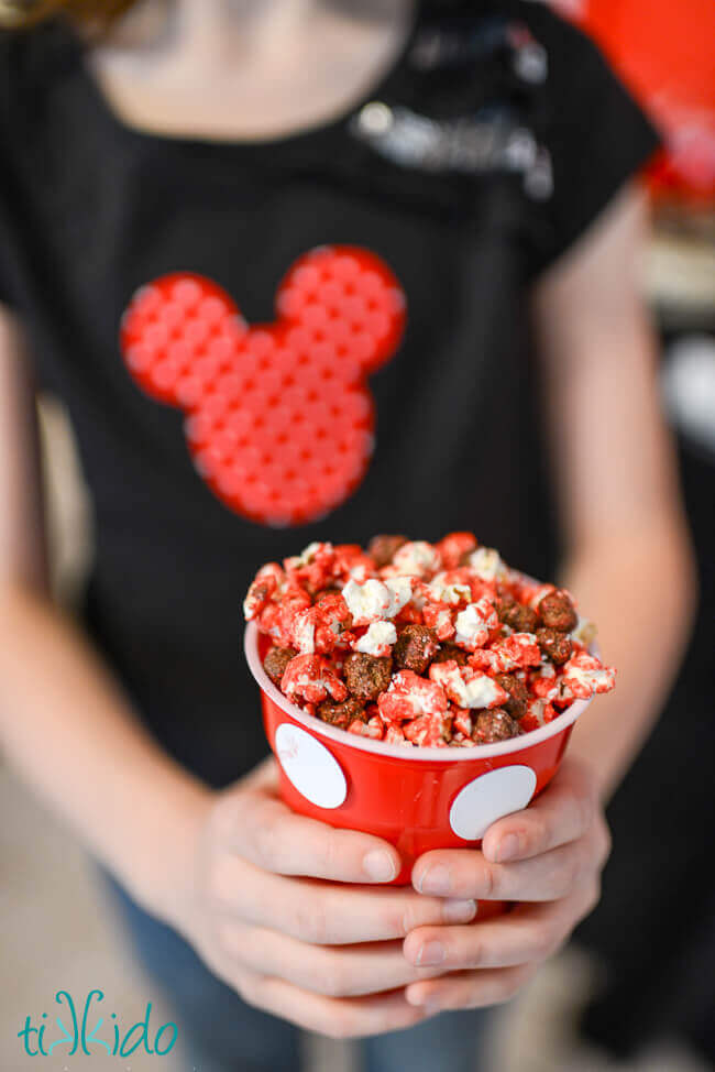 Girl holding a red container full of Mickey Mouse Popcorn.