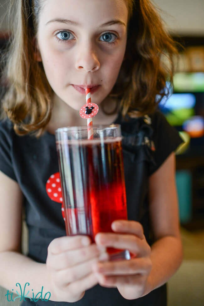 Girl sipping a layered Mickey Mouse drink through a Mickey Mouse straw.
