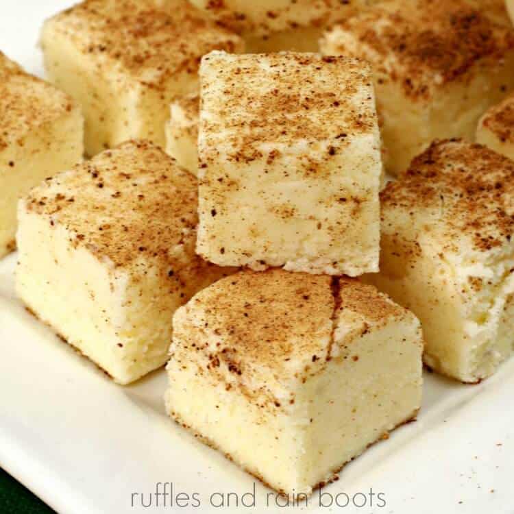 Pieces of eggnog fudge dusted with grated nutmeg on a white plate.