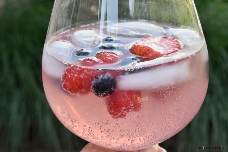Closeup of a wine glass filled with light pink Prosecco punch.  Raspberries, strawberries, and blueberries float in the drink.