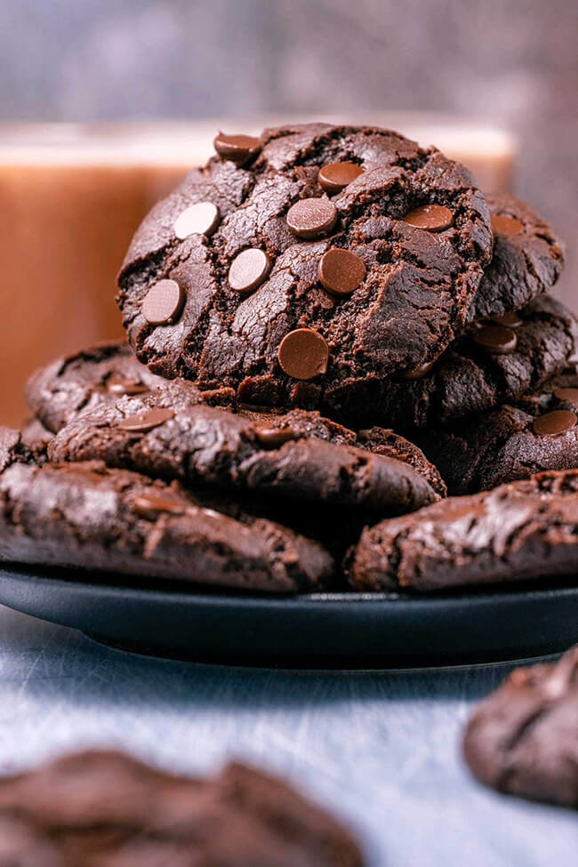 Eggless chocolate chocolate chip cookies stacked on a black plate.