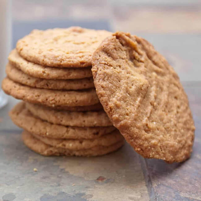 Stack of think, crispy peanut butter cookies on a grey background.