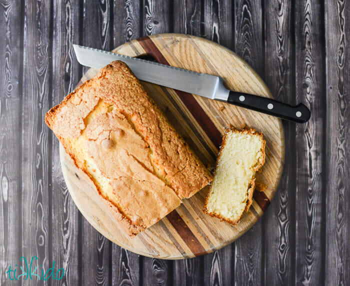 Loaf of pound cake with one slice cut off and a bread knife on a round cutting board on a dark wood surface.