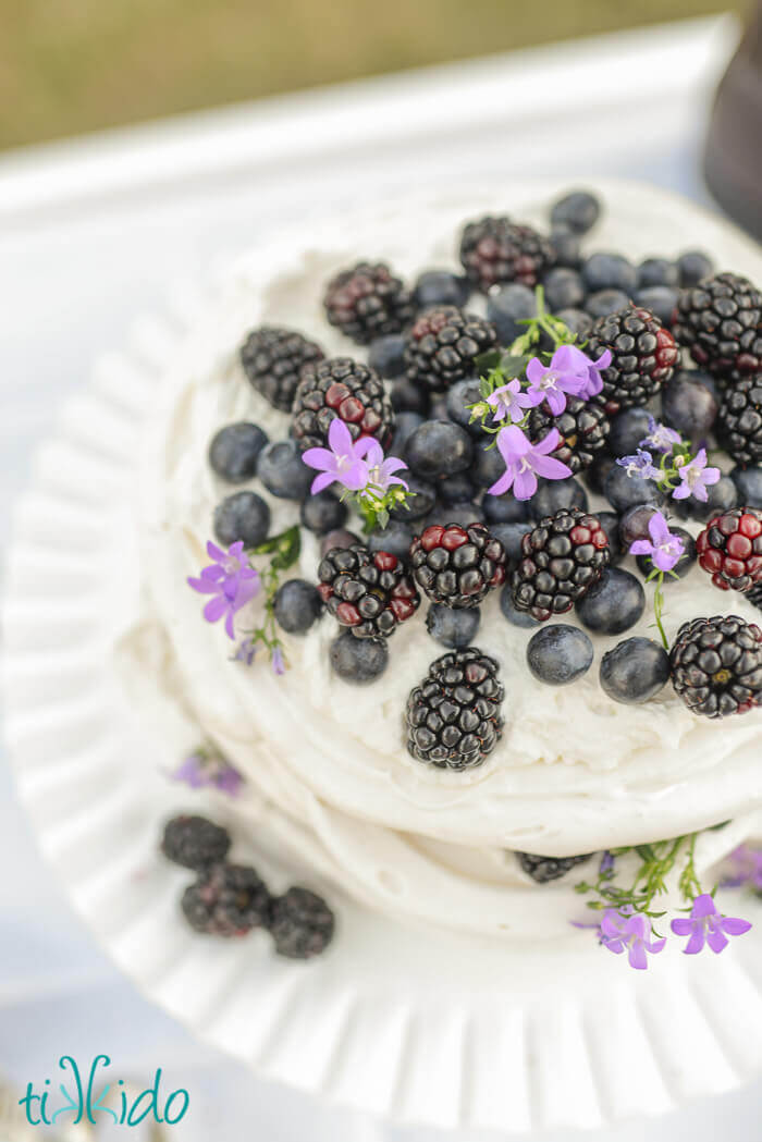 Pavlova layered like a layer cake, topped with whipped cream, blackberries, blueberries, and edible flowers.
