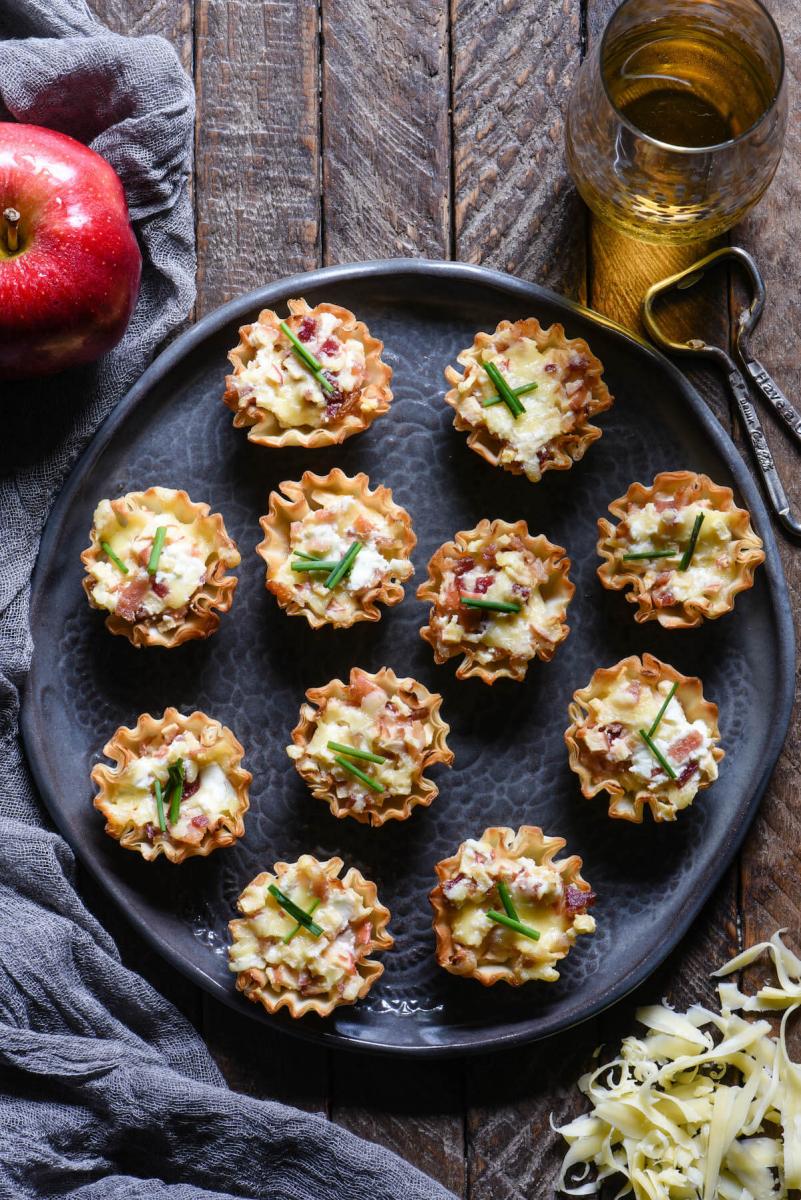 Cheese, apple, and bacon Filo cup appetizers on a round serving tray on a wooden table.