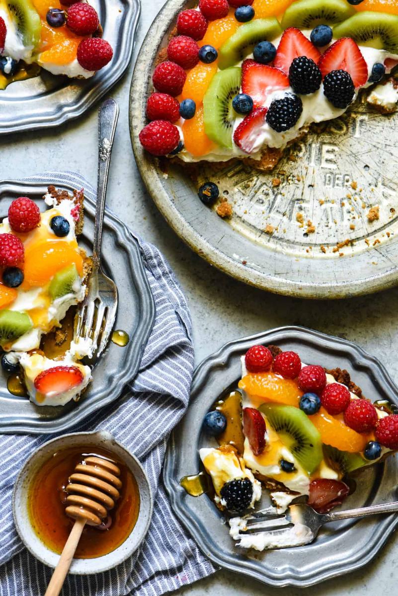 Honey frozen yogurt pie slices on a pie plate, with the rest of the pie still in the pie tin.  The pie is garnished with a rainbow of fruit.