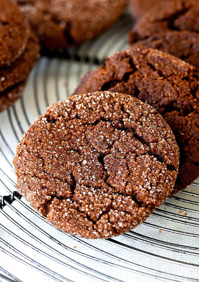 Eggless, Chewy, Ginger Molassas cookies on a wire cooling rack.  The cookies have a crinkled surface, and are baked with coarse sanding sugar coating the tops.