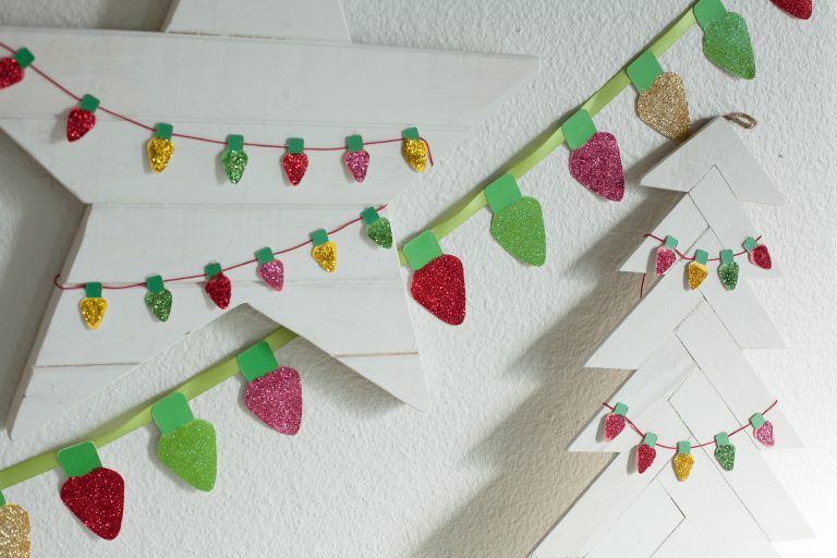 Free printable glitter christmas lights garland hanging on a white wall, and a smaller version of the printable garland strung on white wooden star and Christmas tree decorations.