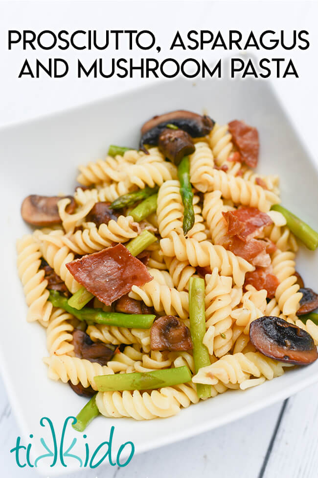 White, square bowl of prosciutto, asparagus, and mushroom pasta.