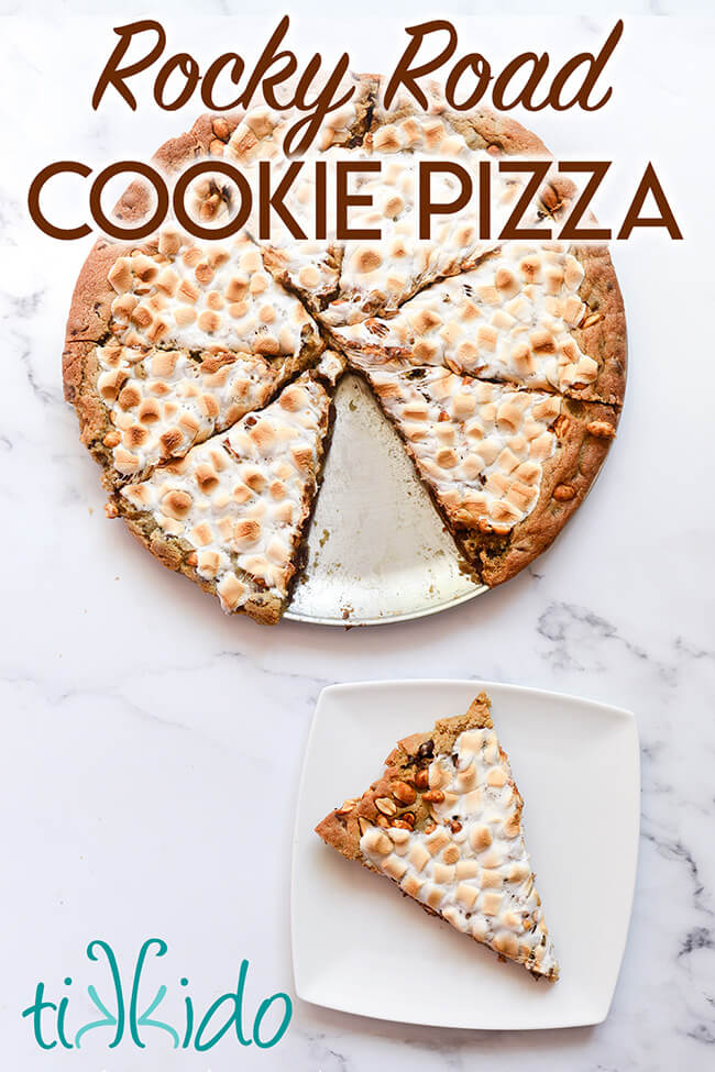 Giant cookie shaped and cut like a pizza, with one slice removed and on a white plate, with text overlay reading "Rocky Road Cookie Pizza."