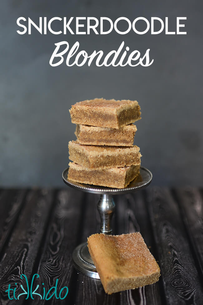 Stack of four snickerdoodle blondies cinnamon sugar bar cookies on a small pedestal.  One square of the snickerdoodle blondies sits askew at the base of the silver pedestal.  Text overlay reads "Snickerdoodle Blondies."