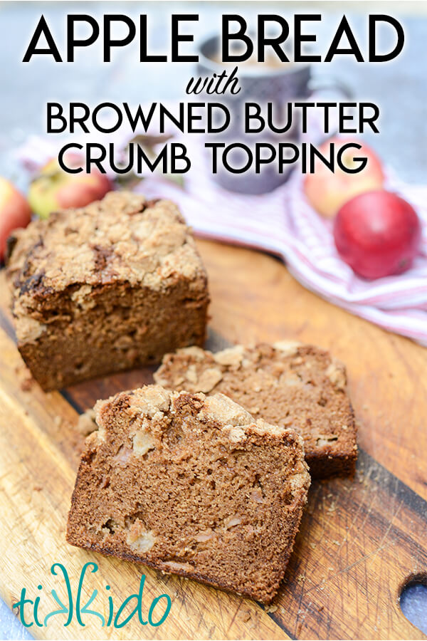 Two slices of apple quick bread cut off of the rest of the loaf on a wooden cutting board, with whole apples, a cup of tea, and a red and white kitchen towel in the background.  Text overlay reads "Apple bread with browned butter crumb topping."