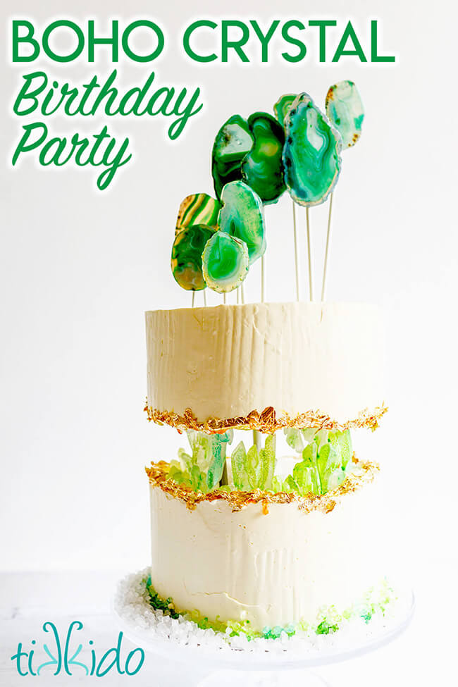 Two tier cake that looks like the top layer is floating several inches above the bottom layer, and green sugar crystals are growing in the center, like a cave or geode.  Green agate slices on white sticks create a modern cake topper.  Text overlay reads "Boho Crystal Birthday Party."