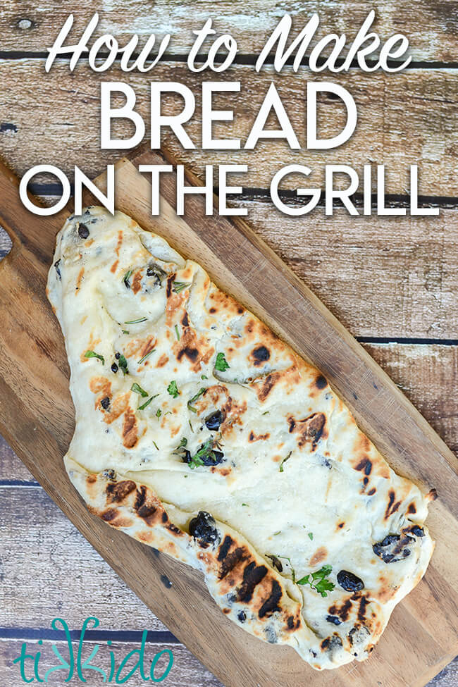Irregularly shaped piece of bread topped with sea salt and herbs, that has been cooked on a grill.  The flatbread sits on a wooden cutting board, and there is text overlay reading "How to Make Bread on the Grill."
